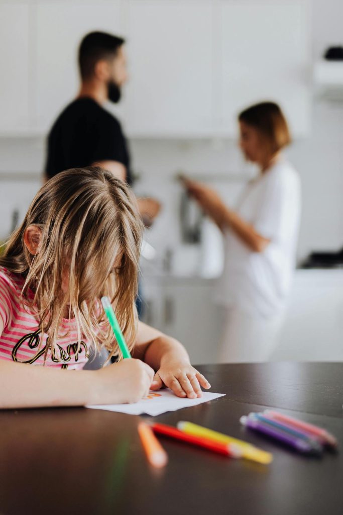 child colouring on a kitchen table while parents discuss in the background
